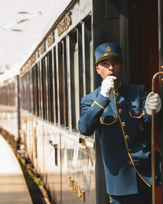 A steward dressed in blue with gold trim blows his whistle as he stands on the carriage step of the departing train