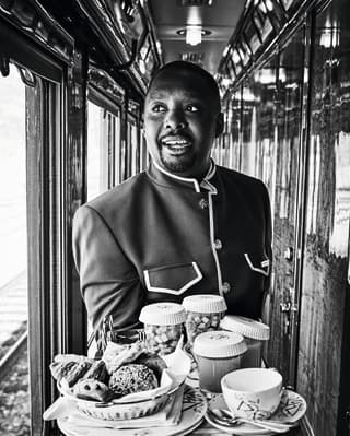 Foto in bianco e nero di un assistente di bordo del treno che attraversa un corridoio stretto di legno