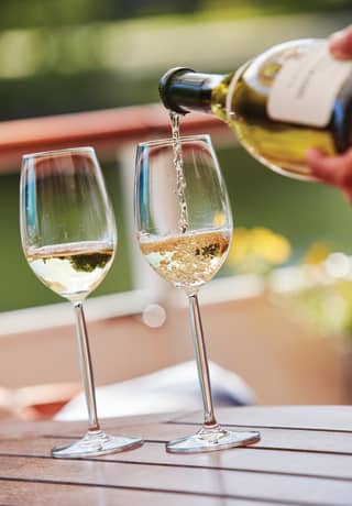 Close-up of white wine being poured from a light green bottle into a glass