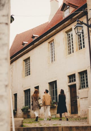 Seen from behind, a male and two female guests take a walk through the quiet and narrow cobbled streets of a Burgundy town.