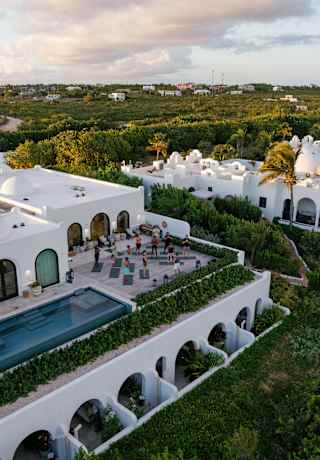 Aerial view of a yoga class, as guests stands on their mats on a second-floor terrace alongside an infinity pool.