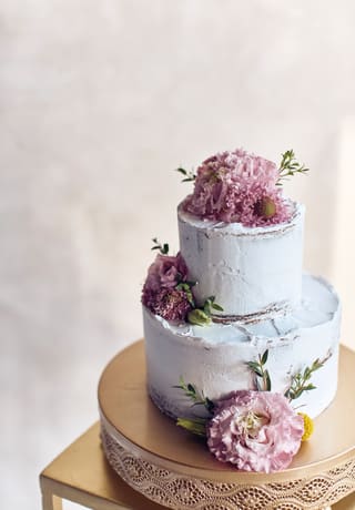 A white two-tiered wedding cake is decorated with fresh cut pale pink Peonies