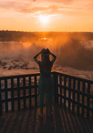 Una mujer admirando las cataratas de Iguazú bajo un amanecer anaranjado