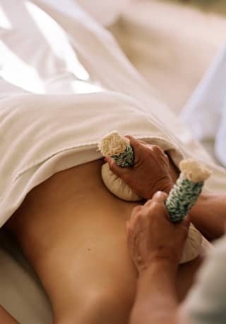A masseuse rubs steam-heated cloth pouches of aromatic and medicinal herbs on the back of a guest during a Pinda Massage.>