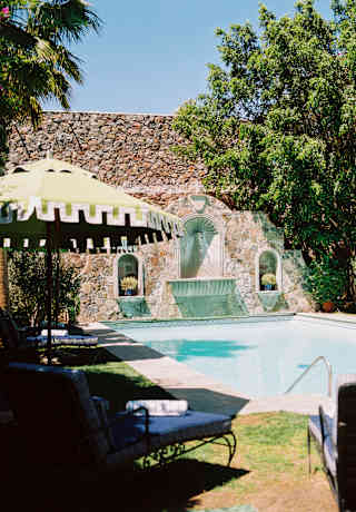 The blue swimming pool glows in sunshine, surrounded by lawn with lounge-chairs and parasols in the hotel's walled garden.