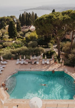Vista aérea de una piscina de hotel al aire libre con exuberantes jardines a lo lejos