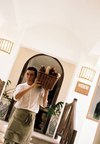 Angled image of a chef with a green waist apron and a woven basket of heirloom corn cobs on his shoulder, outside Woodend.