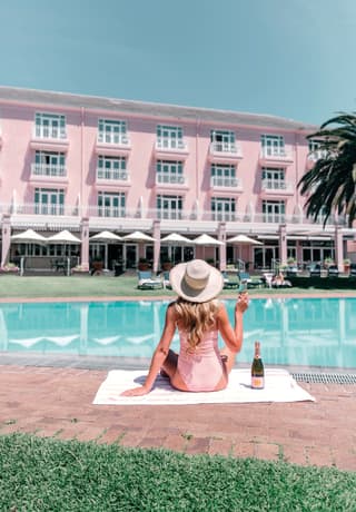 Lady in pink swim suit holding a glass of rosé champagne beside an outdoor pool