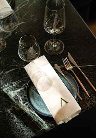 Refracted light through a wine glass makes ringed shadows on a white napkin, laid on a plate with cutlery, seen from above.