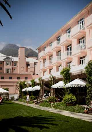 White parasols shade the Oasis terrace, complementing pretty balconies on the hotel's pink façade, viewed from the lawn.