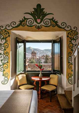 In a Junior Suite bay window with an illustrated border, a red table and two yellow chairs enjoy breathtaking rooftop views.