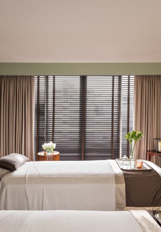 View across the spa treatment room where two beds, with trays of flowers, white sheets and brown satin throws await guests.>