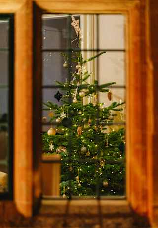 A Christmas tree with lights, decorations and a star brings a festive feel to Le Manoir, seen through a mullion window.