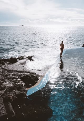 Mujer de pie en el borde de una piscina de agua salada con vista al océano Atlántico