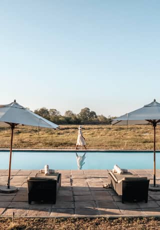 Sunbeds and parasols lining a stone poolside beside an outdoor infinity pool>