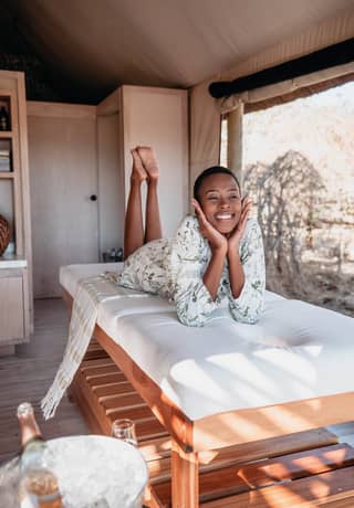 A guest smiles on a spa treatment bed with open views of the bush behind her>