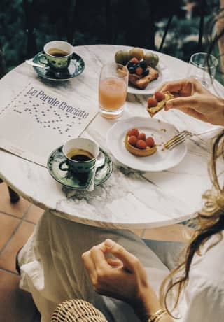 At a La Terrazza breakfast, a female guest enjoys a raspberry tartlet pasticceria with coffee and juice, seen from above.