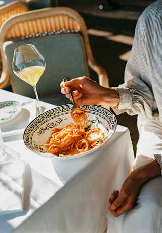 Sunlight falls on a dining table where a guest enjoys spaghetti with rich tomato sauce with a drink at Splendido Grill.
