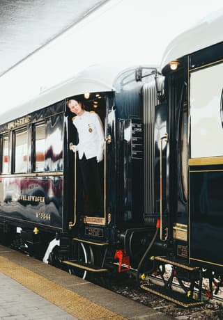 Train steward in a white formal jacket gazing down the exterior of a luxury train carriage
