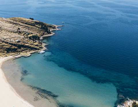 Breathtaking aerial view of the white-sand sweep and clear blue waters of Collata Beach on Lake Titicaca's Taquile Island.