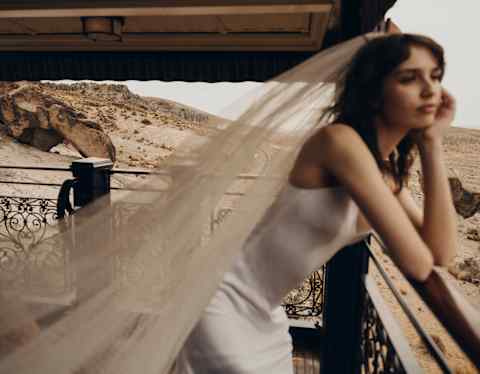 In soft-focus, a bride leans forward on the observation deck rail, propping her chin in a hand as she gazes at the landscape.