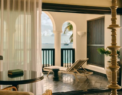Bedroom view on to the balcony with smooth black Arabesque tiles and a sun lounger facing the wide ocean through open arches.
