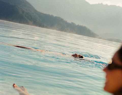 A man swims on his back in the pool, seen over the shoulder of a woman in soft-focus in an image that captures the hill views.