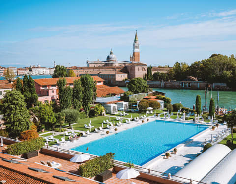 Aerial view of clay tile roofs and an outdoor pool surrounded by sunbeds and parasols