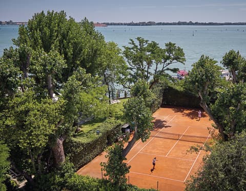 Aerial view of a clay tennis court surrounded by lush garden foliage