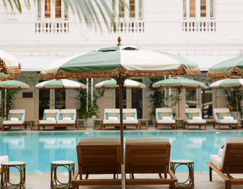 Cream and sage parasols stand to attention beside teak sun loungers that lie ready for guests around a turquoise pool