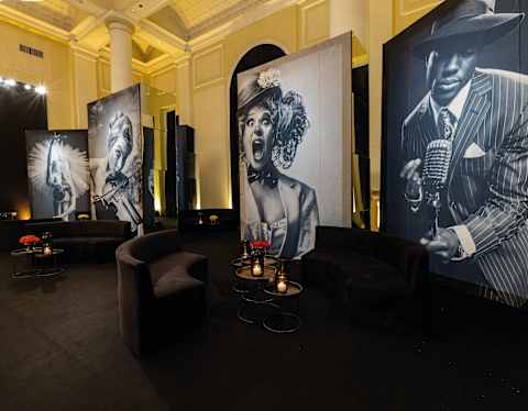 View of a lounge with black banquettes and tables with candles, and large panels with monochrome photographs of entertainers.