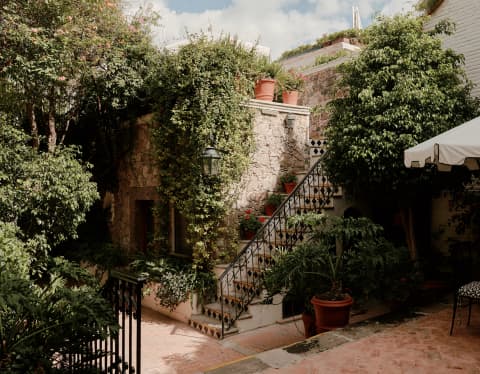 View over the patio at Casa Fuente to an exterior staircase with iron railings, tucked between the ivy-clad stone buildings.