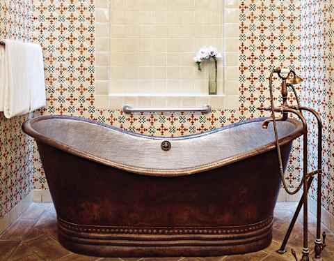 Close-up of a copper standalone bathtub surrounded by red and blue tiles