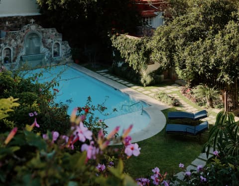 Sun illuminates the sugar-pink spires of Parrocchia San Michele Arcangelo in a high view over the shaded gardens and pool.