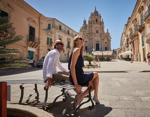 Couple sitting on a bench in an Italian piazza under clear blue skies