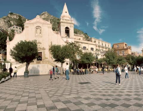 People wander the checked stone floor of Piazza Nove Aprile and sit at cafés by the faded pink stucco church of San Giuseppe.