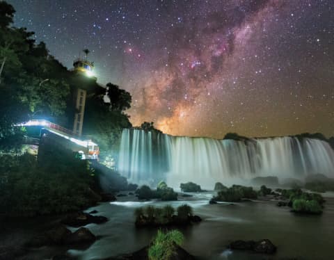 Hyper-produced image of Iguassu Falls' visitor centre and silky, flowing cascades with a starry, pink and blue nebulous sky.