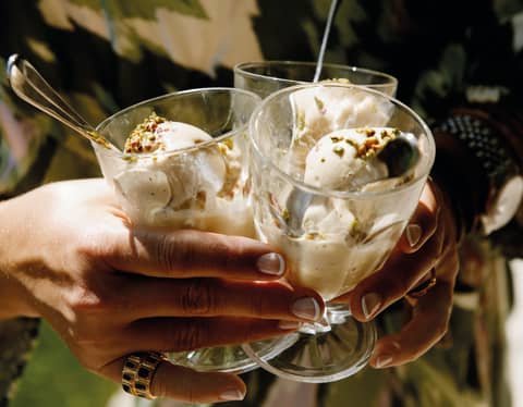 Close-up of a lady's hands clasping three glasses filled with gelato and topped with chopped nuts