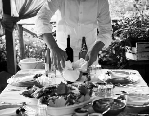 Caruso's Executive Chef Armando Aristarco puts the finishing touches to a table laden with food, shot in black and white.