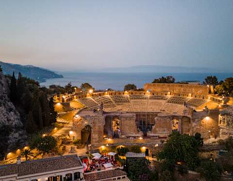 Golden lights dotted around the Teatro Antico di Taormina create a magical arena in the dusk gloom, seen from above.