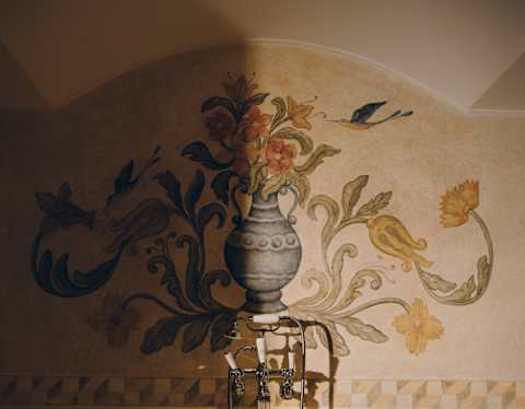 A painterly mural of a flower urn bursting with leaves and blooms, seen on the wall behind a marble bath in a suite bathroom.