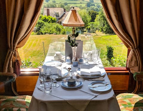 A crisp white tablecloth covers a window table set for two, with glorious views of the green fields of the English countryside