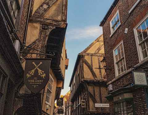 View of The Shambles in York where ancient beamed buildings lean, heads almost together, over a medieval cobbled lane.