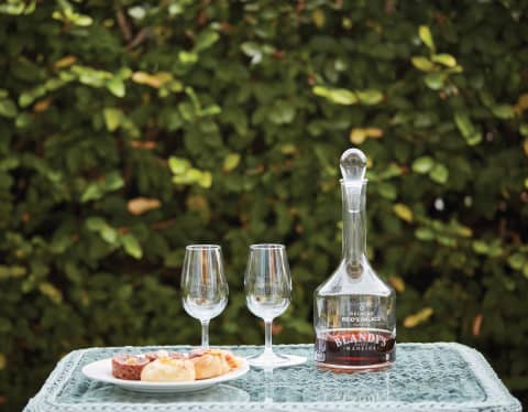 Madeira wine in a glass decanter with two wine glasses and a cake platter on a tray