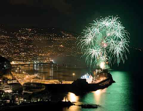 White and green star-cluster fireworks light up the night sky above Funchal marina, casting a peppermint hue on the water.