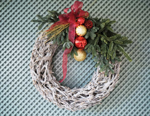 A simple and tasteful Christmas wreath made with latticed wood, fir sprigs and gold and red baubles, tied with red ribbon.