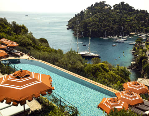 Terracotta parasols pepper the sun terrace beside the aquamarine pool. Far below the wooded cliff, yachts moor in the harbour