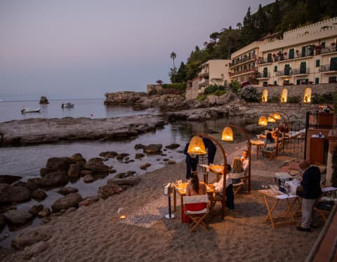 Diners are served on a private beach, their tables illuminated under private pools of light from tulip-shaped lamp stands