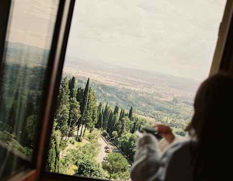 Angled shot of a guest in soft-focus as she gazes at the beautiful vista of Florence's hills and roofs from an upper window.