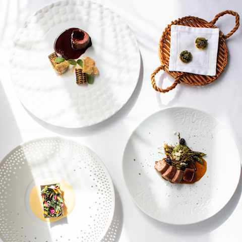 A selection of Chef Costa's amuse-bouches and signature dishes served on four white plates, a floral bed and a wicker basket.